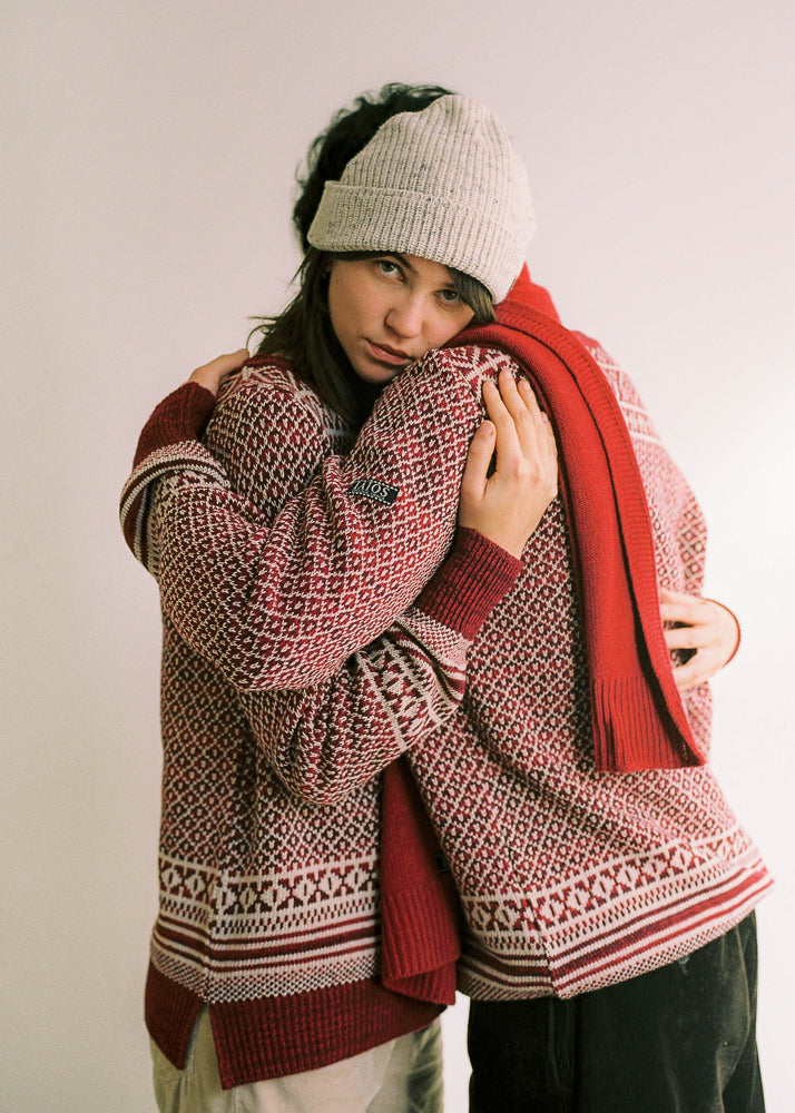 Dos modelos abrazados con el jersey de mujer IAIOS rojo y blanco con jacquard navideño, detalle del tejido, moda sostenible elaborada con hilo reciclado en talleres de Catalunya (España).