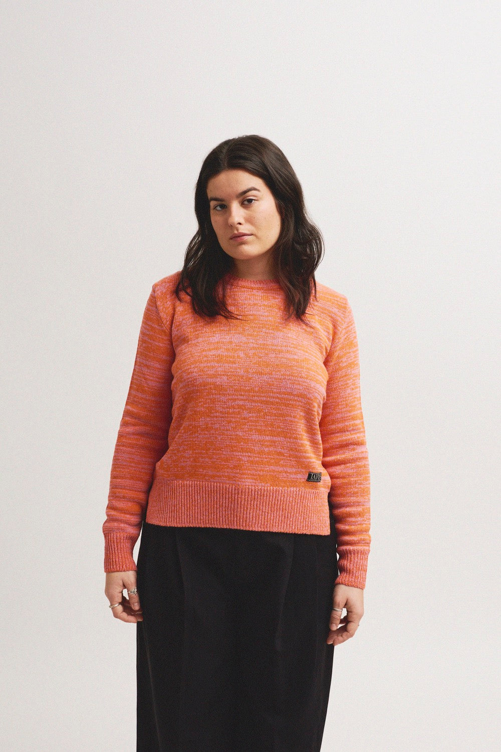 La modelo lleva el jersey unisex IAIOS salmón liso, mezcla de hilos rosas y naranjas, patrón básico y recto, moda sostenible hecha en Catalunya (España) con hilo reciclado.