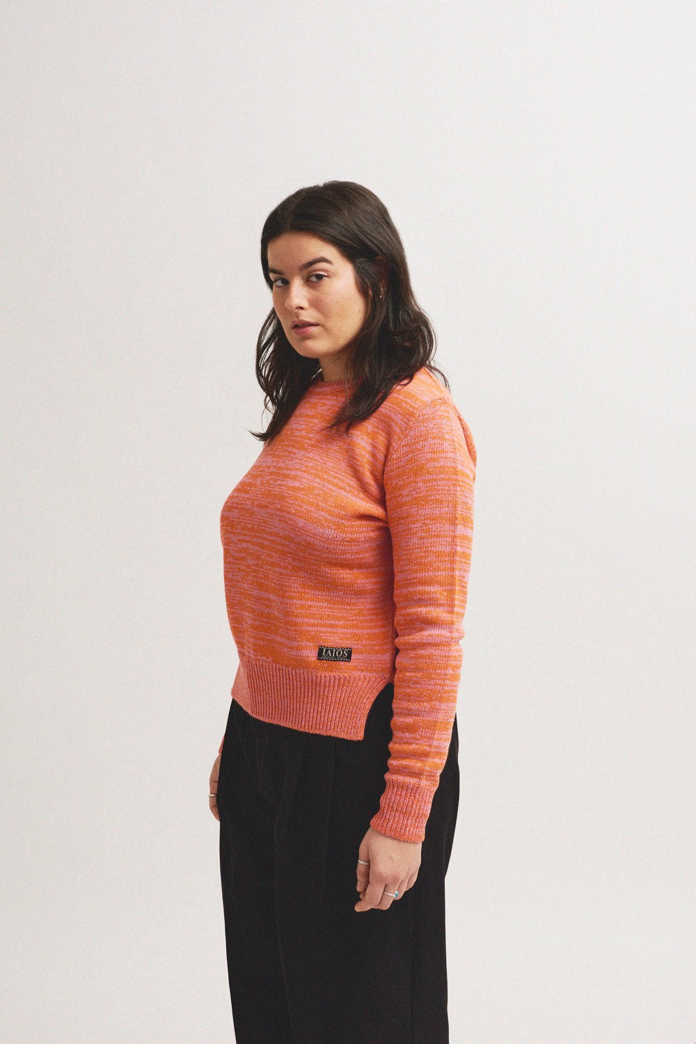 El modelo lleva el jersey IAIOS salmón liso unisex, mezcla de hilos rosas y naranjas, moda sostenible elaborada en talleres de Catalunya (España) con hilo reciclado.