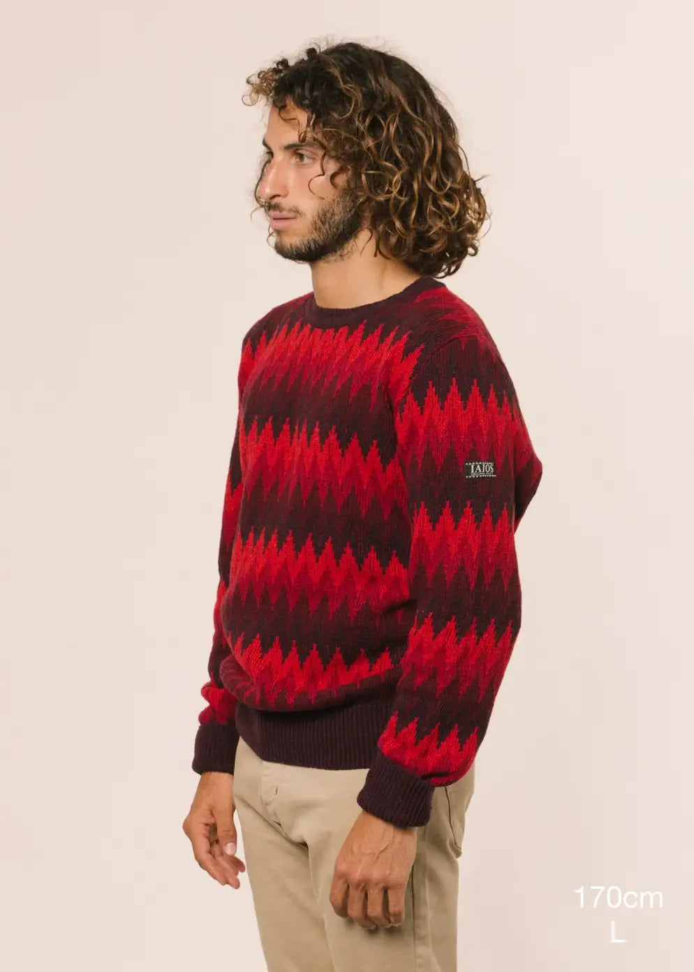 El modelo lleva el jersey unisex IAIOS de tres colores con diseño en zigzag efecto espiga en tonos rojizos, moda sostenible hecha en Catalunya (España) con hilo reciclado.