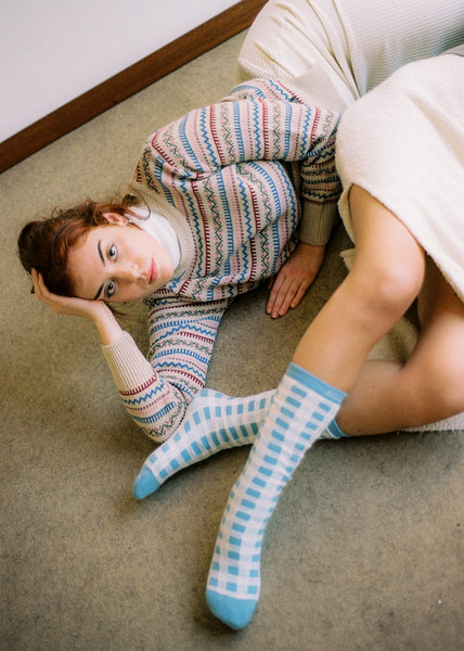 Staged photograph, stretched woman with sweater and white skirt.