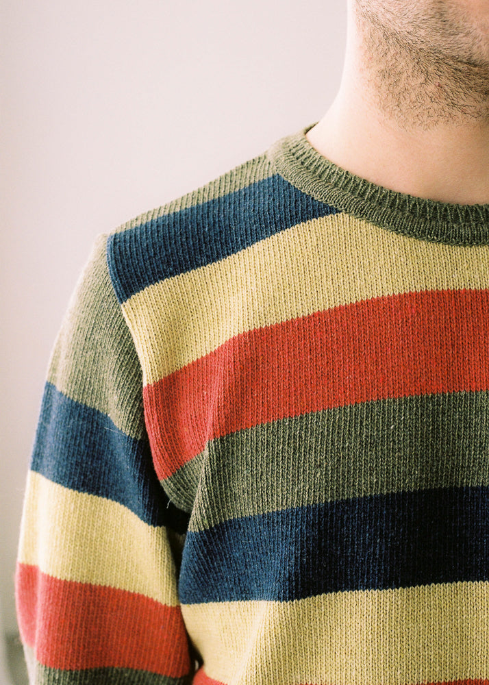 Fotografia de detall del jersei en la qual aprecien els seus colors; verd caqui, blau marí, Groc clar i taronja fosc.