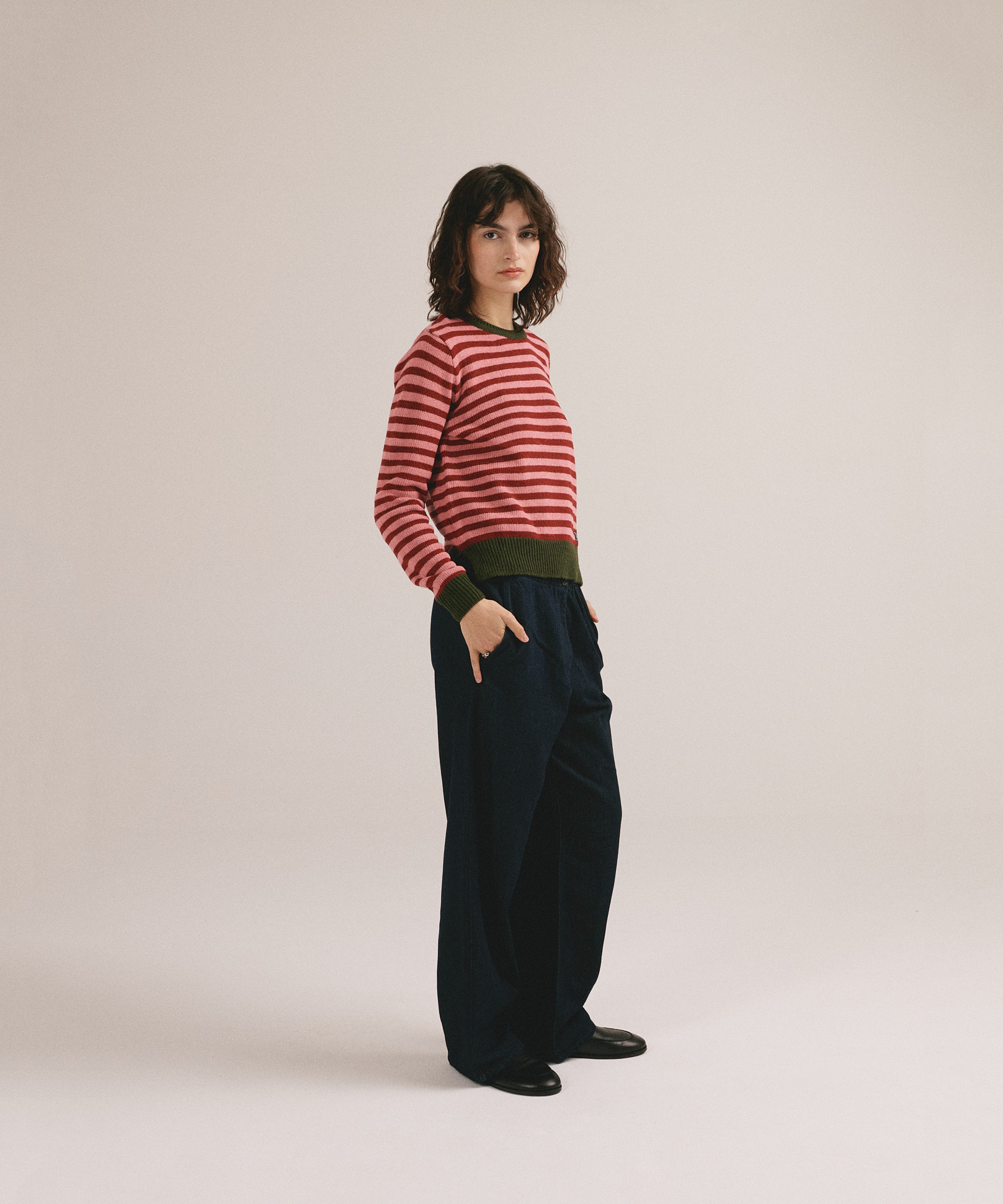 Modelo femenina con suéter de punto de rayas en tonos rojo y rosa con cuello y puños verdes de IAIOS.