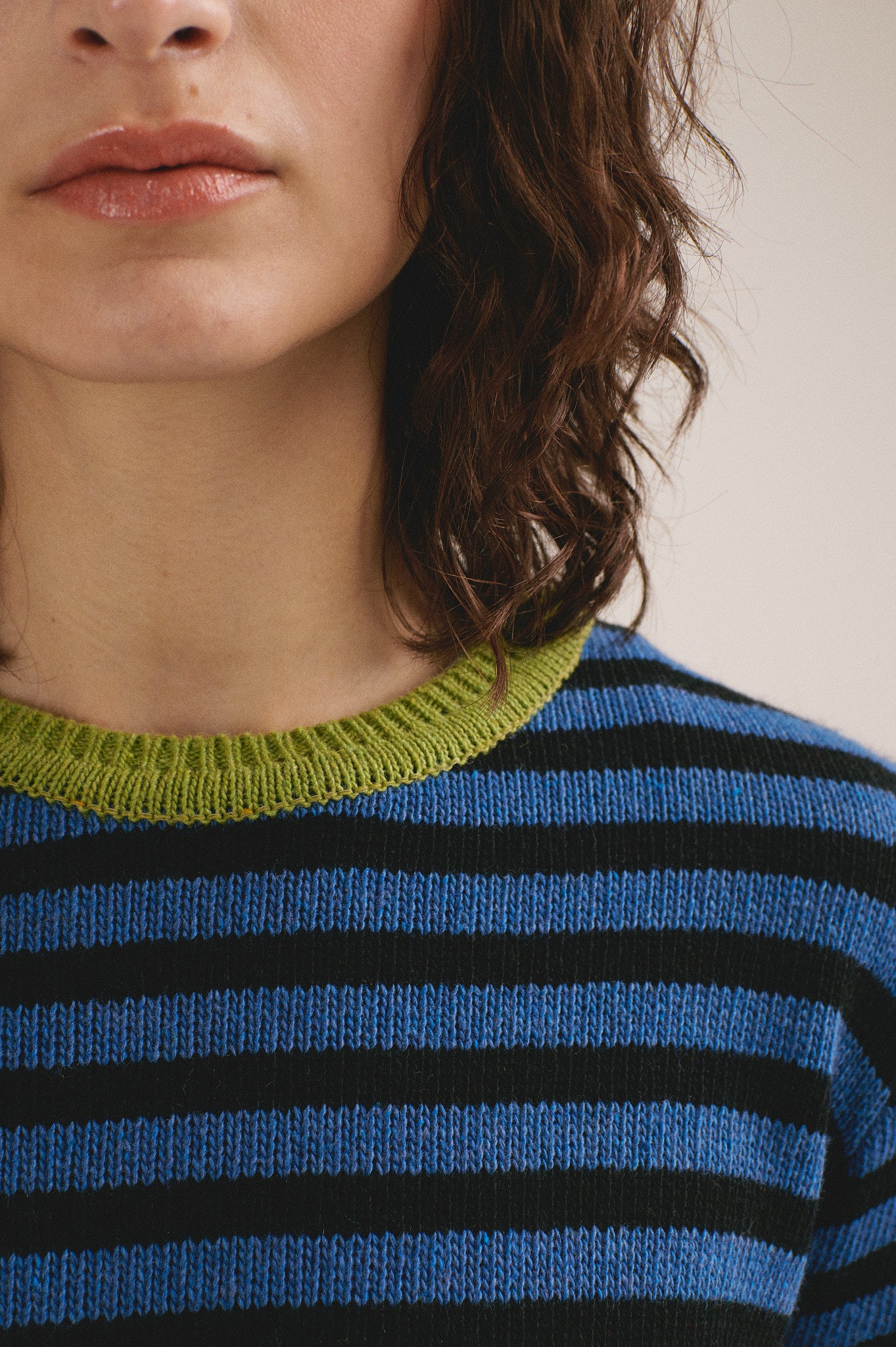 Detalle del cuello del jersey de punto para mujer con diseño de rayas bicolor y acabados en verde, look de otoño invierno.