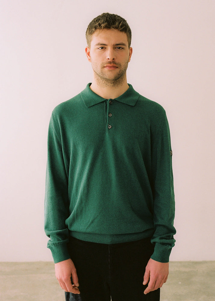 Fotografía de medio cuerpo, modelo (masculino) lo lleva combinado con pantalón oscuro. El modelo lleva el polo IAIOS unisex verde de algodón reciclado, con cuello clásico y botones, moda sostenible elaborada en talleres de Catalunya (España).