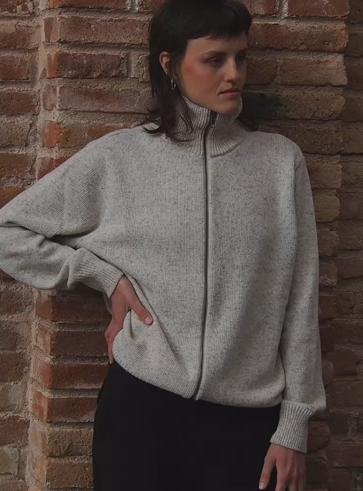 Modelo con jersey unisex IAIOS blanco jaspeado con cuello alto y cremallera completa, ajuste relajado, hecho en Catalunya (España) con hilo reciclado.