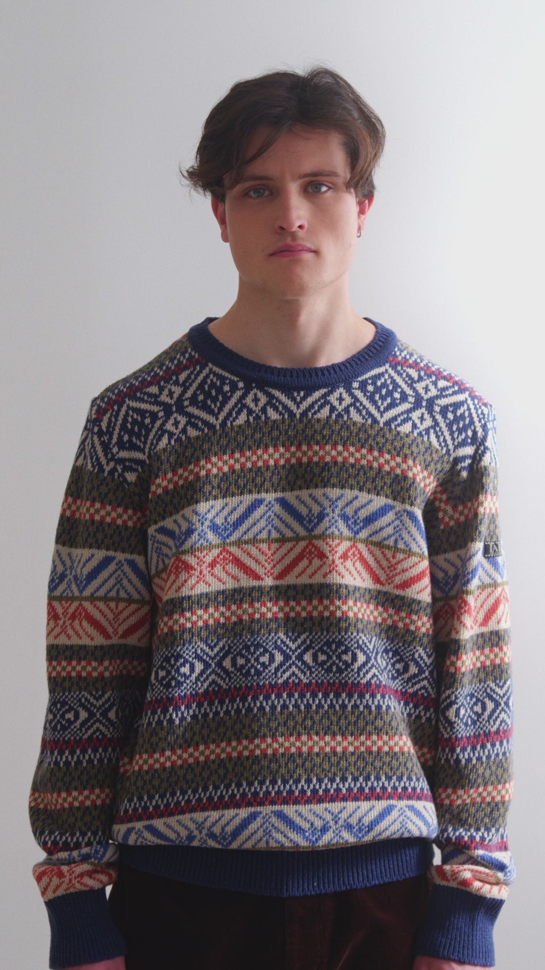 Video en el que el modelo lleva el jersey de hombre IAIOS con motivos invernales tipo nórdico en colores azul marino, blanco y naranja, moda sostenible hecha en Catalunya (España) con hilo reciclado.