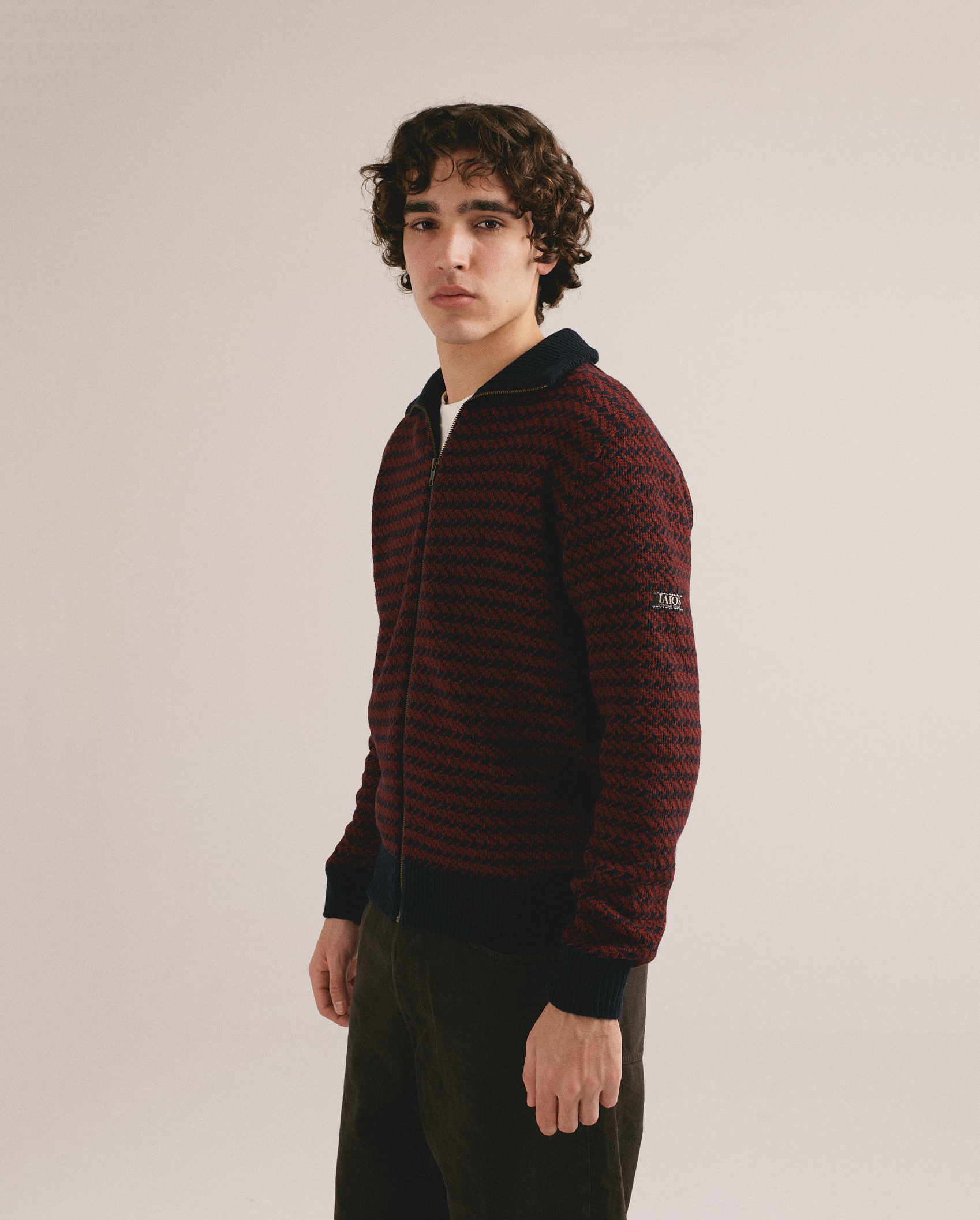 Hombre joven vistiendo cárdigan de punto con cremallera en tonos rojo y negro y estilo casual moderno.