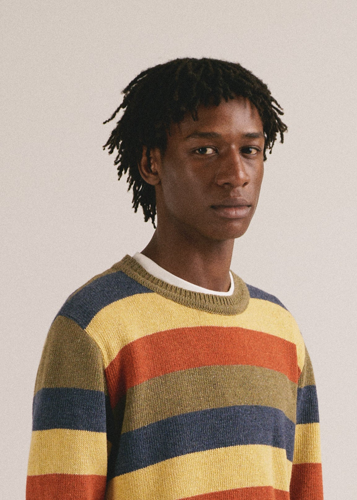 Hombre joven vistiendo jersey de punto a rayas multicolor con estilo casual moderno.