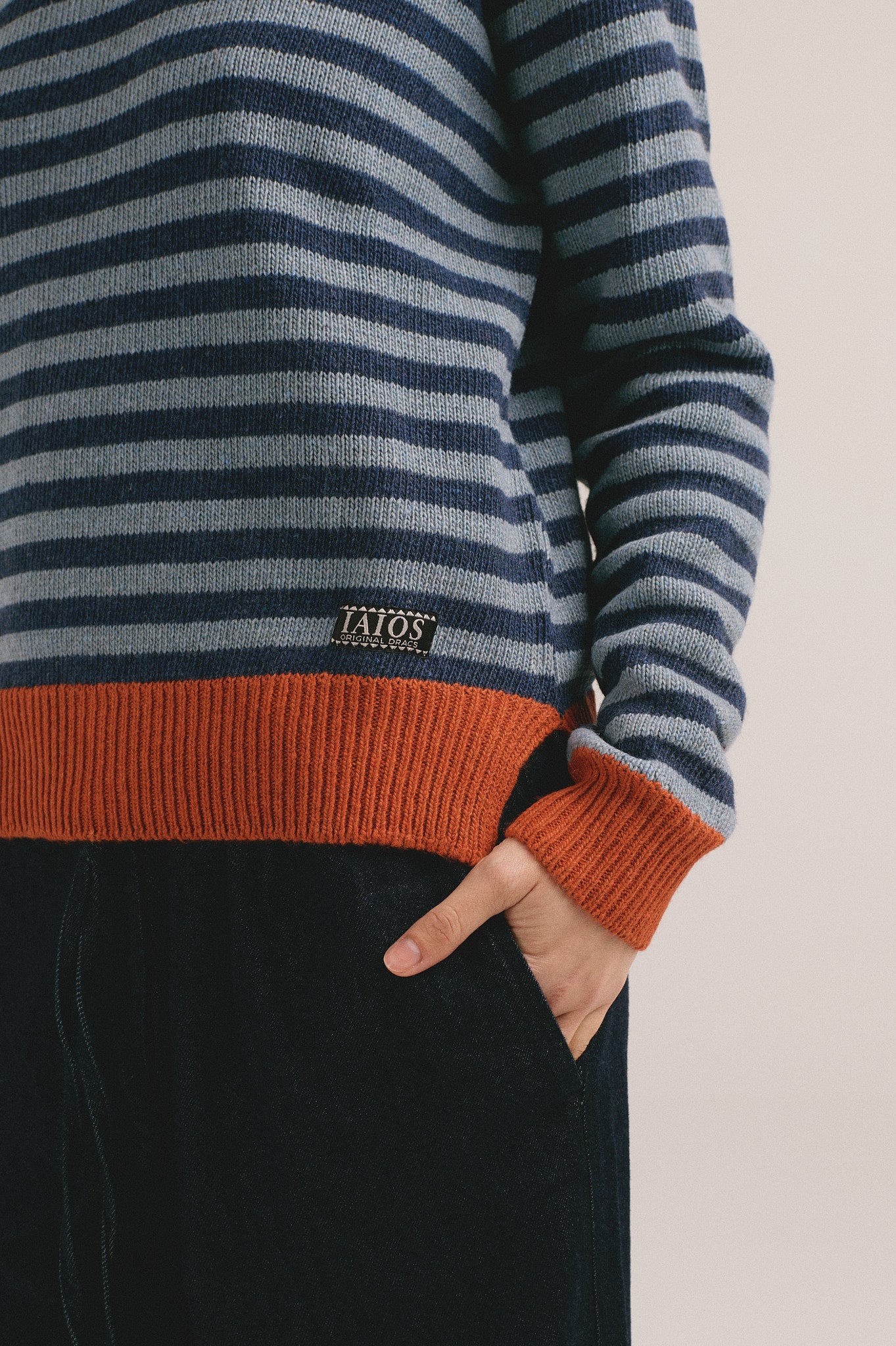 Detalle del jersey de punto para mujer con diseño de rayas bicolor y acabados en naranja, look de otoño invierno.