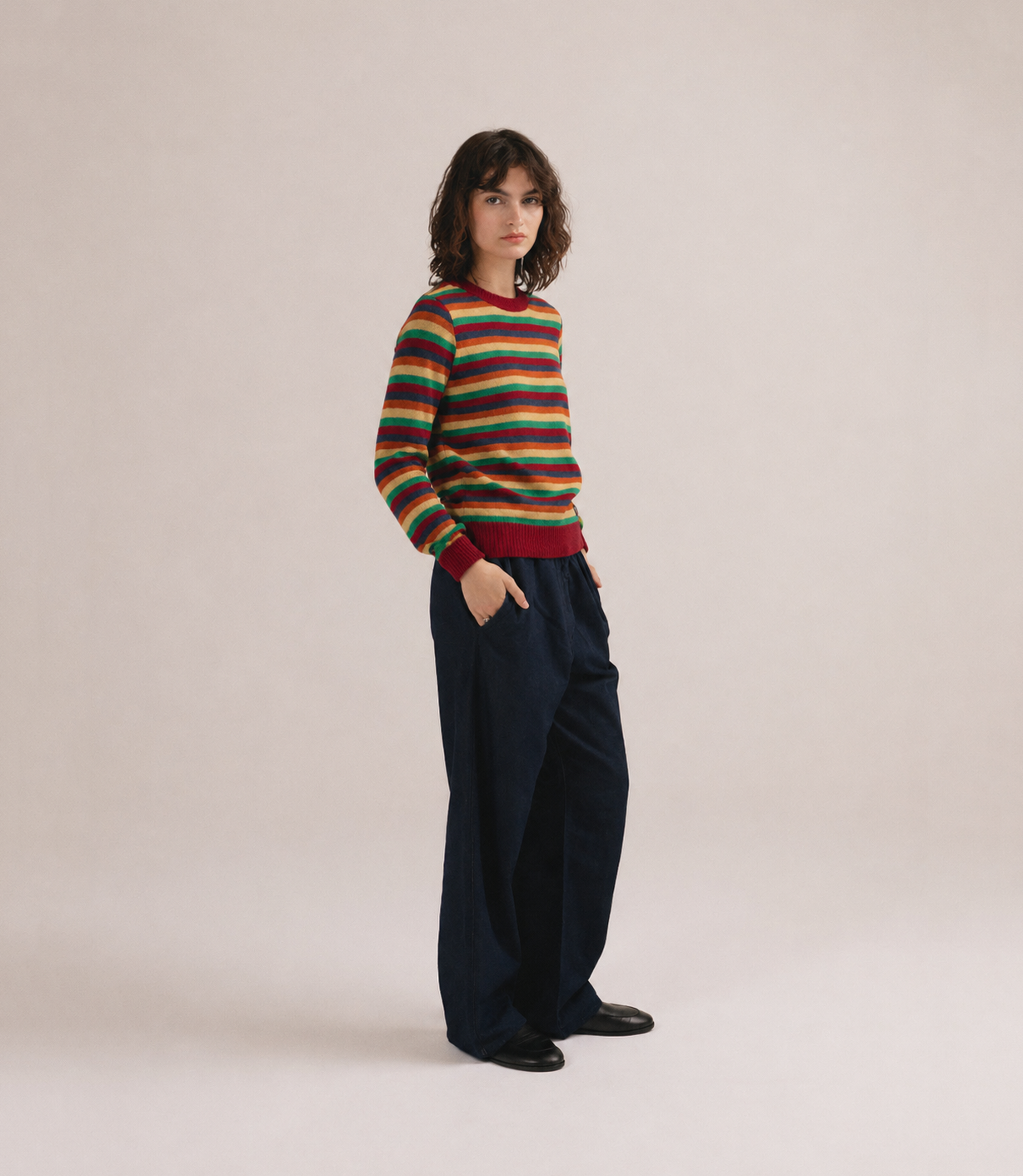 Mujer con jersey de punto a rayas multicolor con detalles rojos de IAIOS y pantalón oscuro.