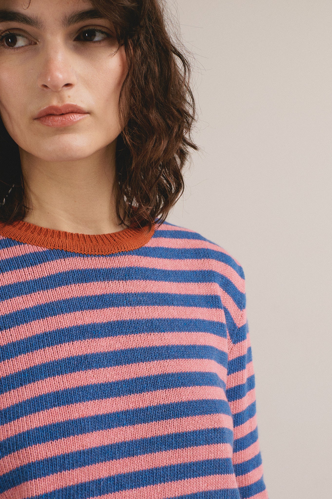 Modelo femenina con suéter de punto de rayas en rosa y azul con cuello y puños naranjas de IAIOS.