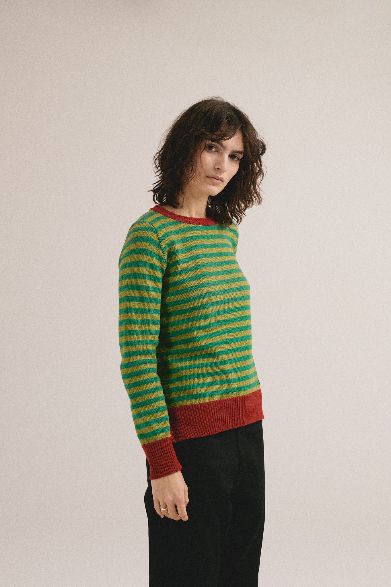 Modelo femenina con suéter de punto de rayas en verde y mostaza con cuello y puños rojos de IAIOS.