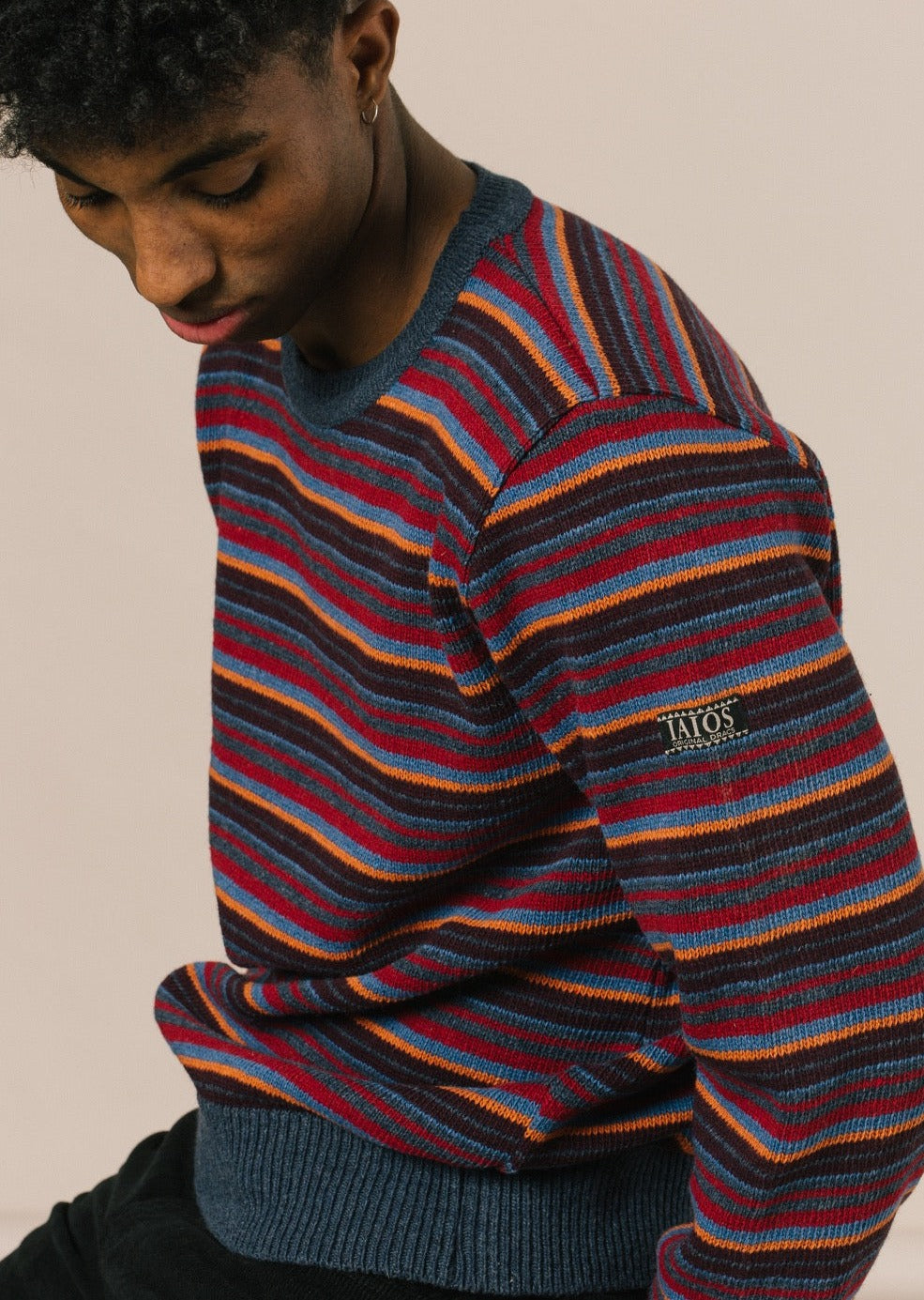 Modelo sentado con el jersey que es un diseño clásico y atemporal que no pasa de moda. Por sus tonos azules y rojos favorece mucho y es perfecto para llevar en cualquier ocasión, como en el trabajo o la montaña.