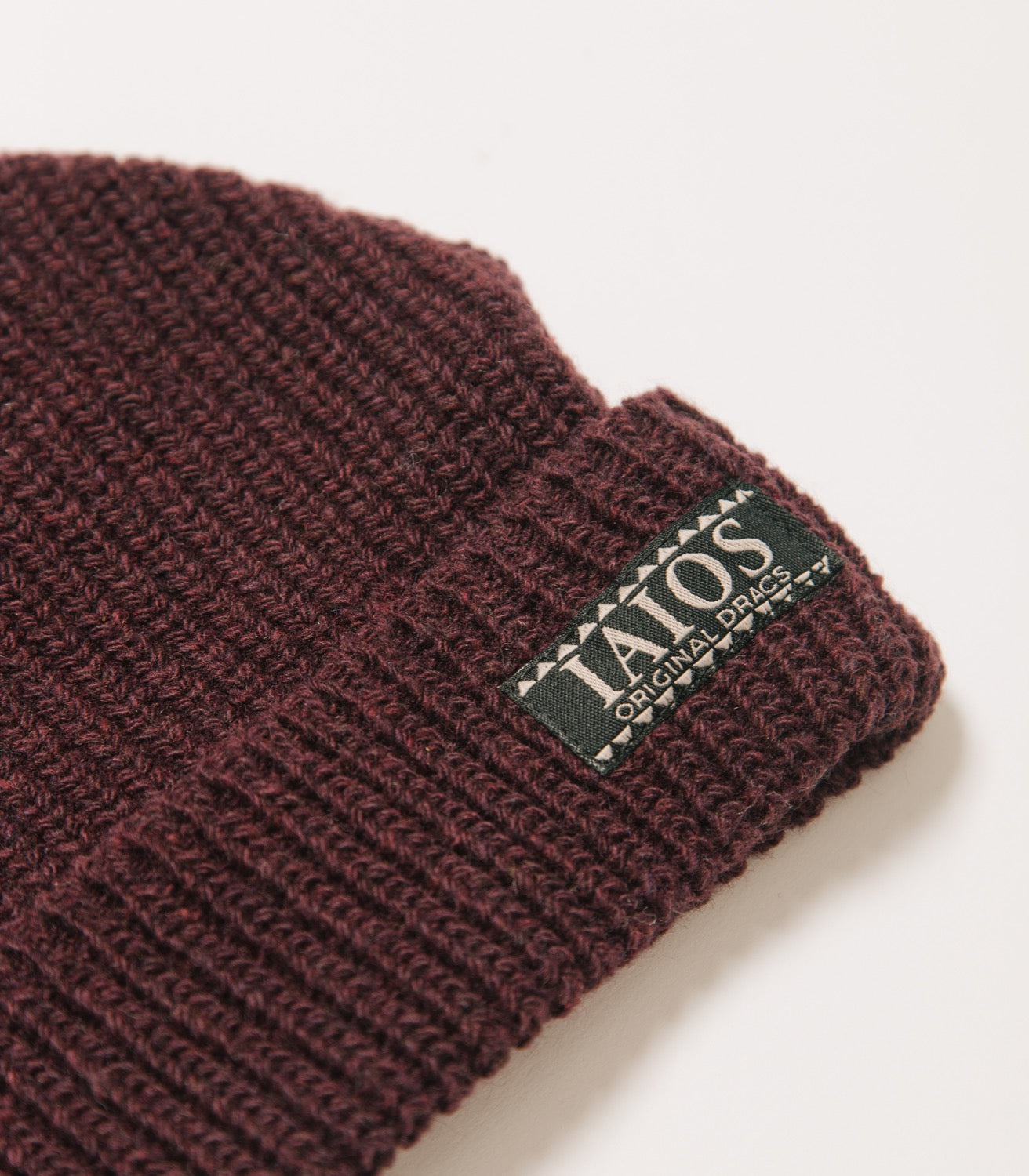 Detalle de la etiqueta IAIOS que lleva el gorro color vino..
