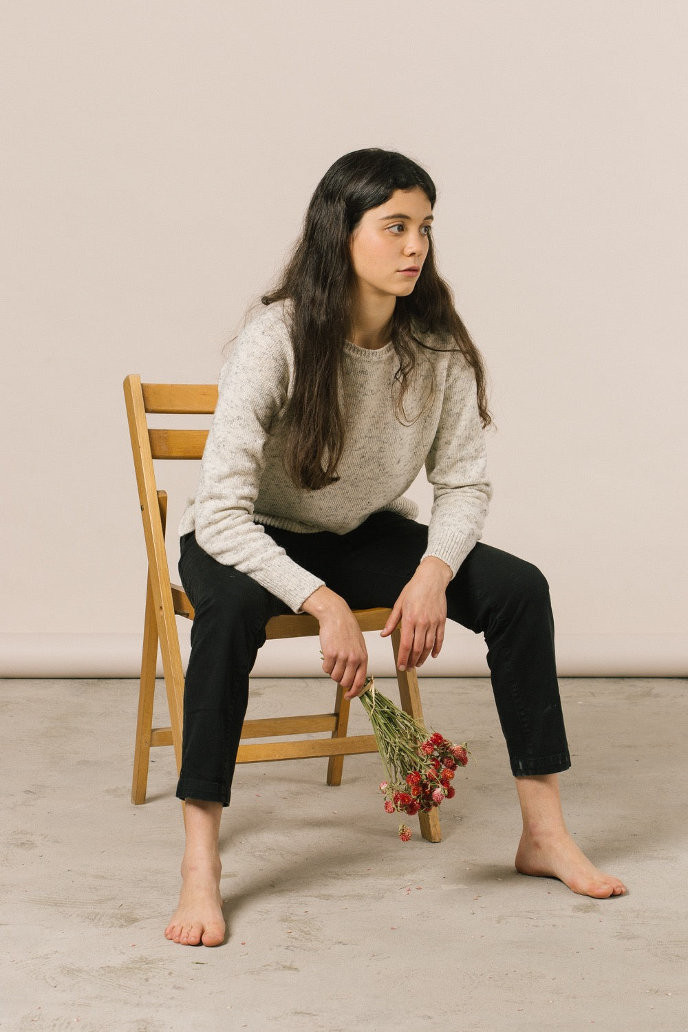 Modelo sentada en una silla de madera con unas flores rojas en la mano.