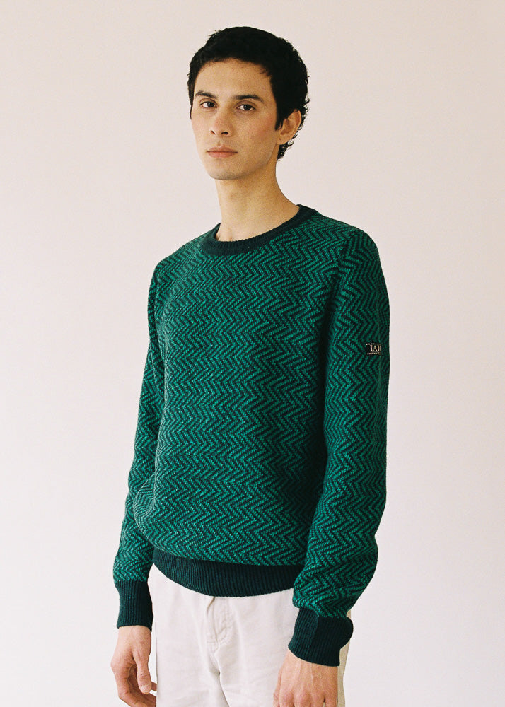 El modelo lleva el jersey unisex IAIOS verde con diseño de zigzag, moda sostenible hecha en Catalunya (España) con hilo reciclado, ideal para invierno.