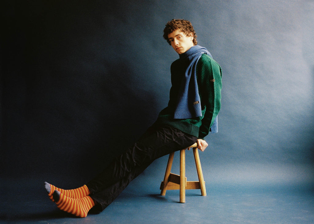 El modelo lleva el jersey unisex IAIOS verde con diseño de zigzag, moda sostenible hecha en Catalunya (España) con hilo reciclado, ideal para invierno.
